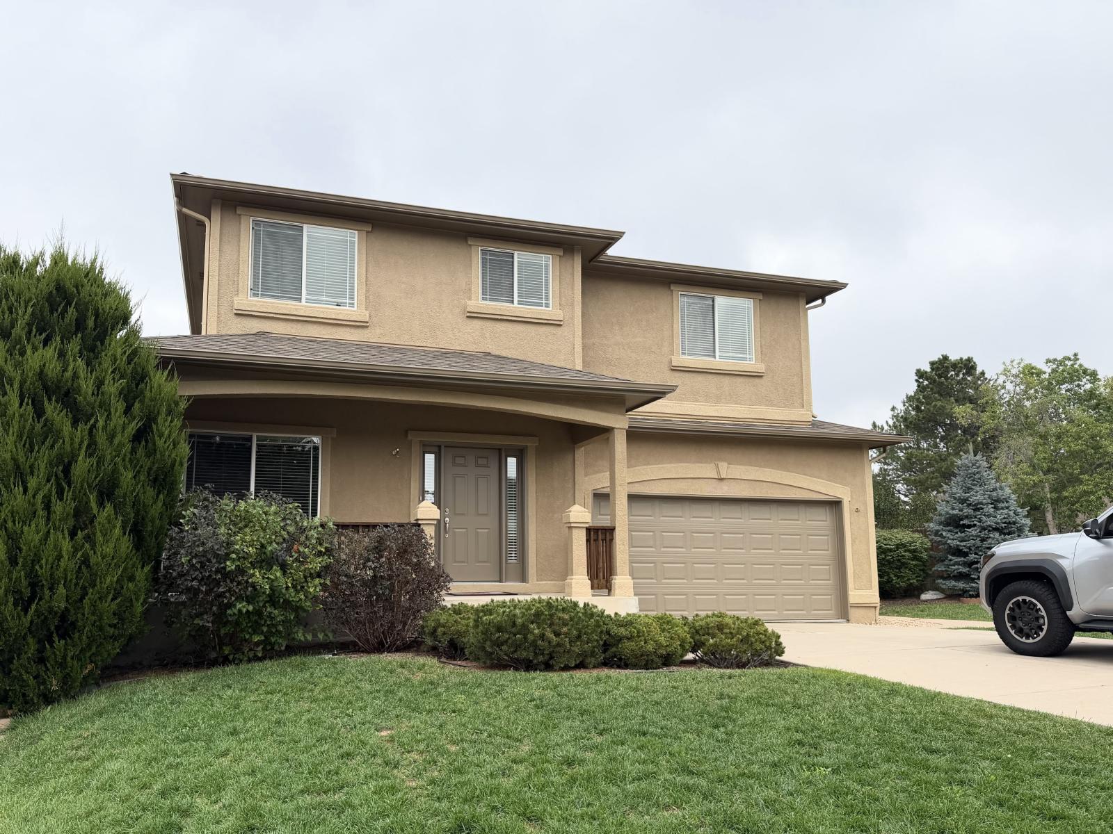 After: the same front elevation recoated in warm khaki with dark bronze gutters, doors and garage door
